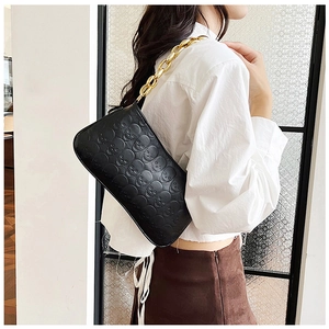 Detail of black underarm bag featuring skull embossing and a chunky gold chain strap