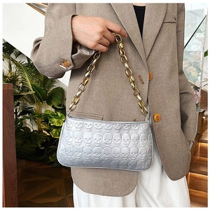 Detail of silver skull embossed handbag with chunky gold chain strap over the shoulder
