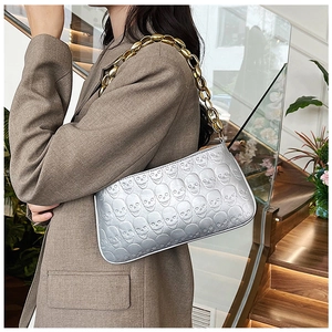Close-up of silver skull embossed handbag with thick gold metal chain strap on shoulder