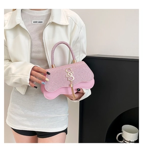 Détail d'un sac à main rose scintillant avec bords ondulés et lettre S dorée en métal