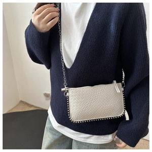 Detail of white crocodile-embossed crossbody bag with silver studs and chain strap