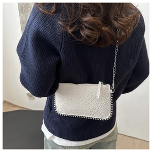 Detail view of white chain bag with crocodile texture and silver stud trim on the bottom