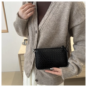 Detail of black woven texture crossbody bag with silver studs and chain strap