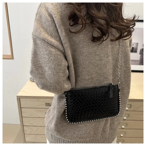 Detail of black woven shoulder bag with silver chain strap and studded trim edge