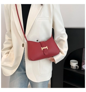 Détail du sac porté épaule rouge mat avec boucle H dorée sur une veste blanche