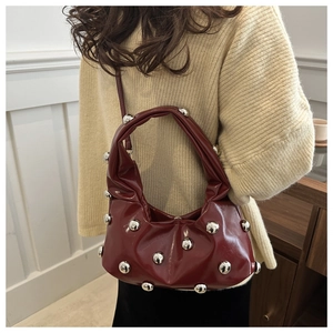 Close-up of wine red glossy leather baguette bag with silver stud rivets on beige sweater