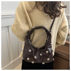 Detail of dark brown shoulder bag with silver studs worn with a beige sweater