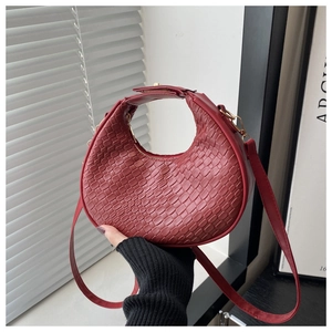 Detail of dark red woven crescent handbag showing faux leather texture and top handle