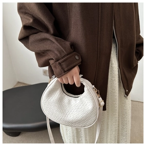 Close-up of white woven crescent bag with adjustable strap and golden hardware