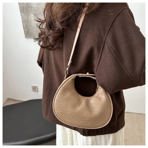 Detail of beige crescent crossbody bag with crocodile pattern worn by a model