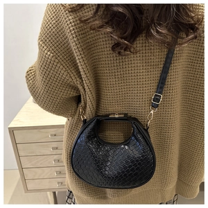 Detail of black crescent shoulder bag with woven texture on a brown knit sweater