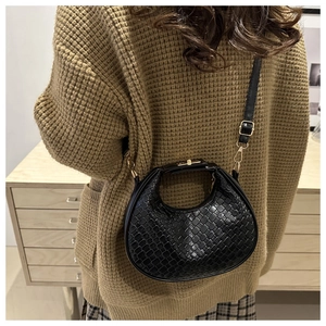 Detail of black woven leather crescent bag with gold hardware worn over a brown knit sweater