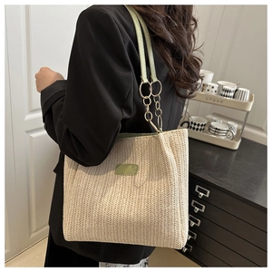 Detalle del bolso tote de paja tejida con parche de cuero verde y eslabones de cadena oro