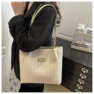 Dettaglio della borsa tote in paglia intrecciata con finiture verdi e catena d'oro