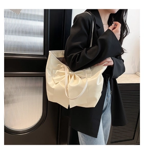 Detail of a large creamy white leather tote bag featuring a decorative bow on the shoulder
