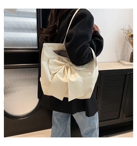 Détail d'un grand sac cabas crème avec nœud décoratif porté à l'épaule du modèle