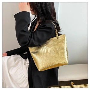 Chic gold crocodile pattern tote bag with metal chain strap worn by a female model