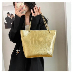 Macro detail of glossy crocodile pattern texture and gold chain strap on tote bag