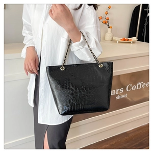 Detail of black crocodile texture tote bag with gold chain strap in a cafe setting