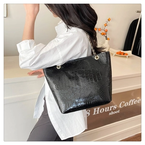 Close-up of black crocodile pattern tote bag with golden chain strap in a cafe setting