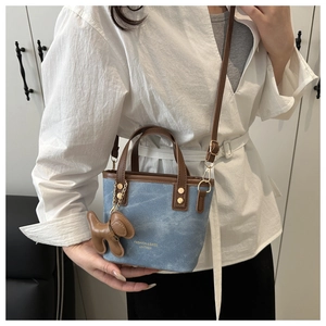 Detailed shot of a color-block denim bucket bag with brown leather handles and gold hardware