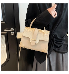 Detail of beige faux crocodile leather shoulder bag on model with gold clasp accents