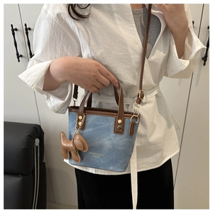 Detalle de bolso cubo en lona azul y cuero marrón con colgante de perro en modelo