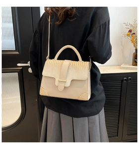 Detail of beige shoulder bag with crocodile texture and gold bar on a model's back