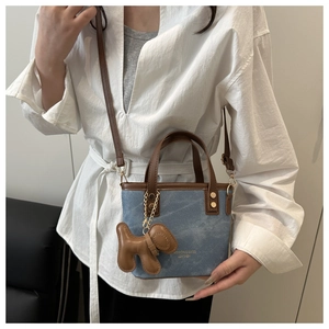 Detail of contrast stitch denim and brown leather bucket bag with puppy charm accessory