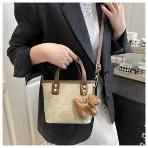 Detail of khaki canvas tote bag with leather trim and cute puppy charm accessory