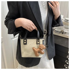 Detail of canvas bucket bag with black leather trim, gold studs, and puppy charm