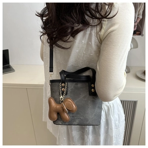Detalle de bolso bandolera de lona gris con asa negra y colgante de perro de color marrón