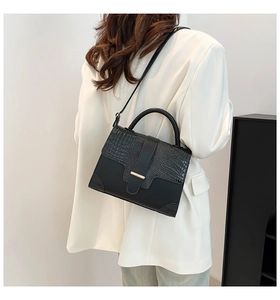 Detail of elegant black crocodile pattern handbag with gold clasp on white blazer