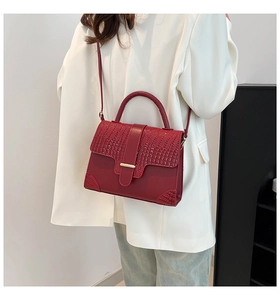Detail of dark red handbag with crocodile texture and metal buckle on ivory blazer