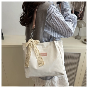 Detail of off-white tote bag featuring lace bow and pink strap with chain link