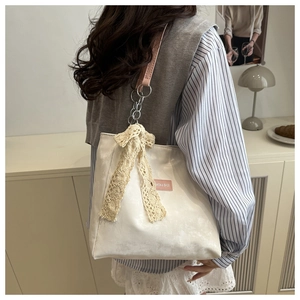 Close-up of cream corduroy tote bag with lace bow charm and pink chain strap detailing