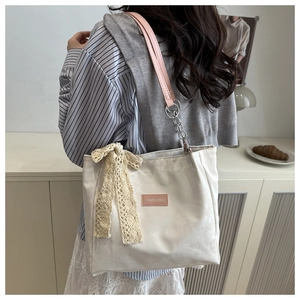 Detail of cream tote bag featuring pink straps and elegant lace bow decoration