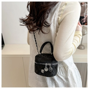 Detail of black quilted mini cylinder bag featuring metal chain and camellia charm
