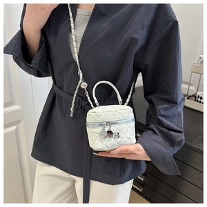 Détail d'un sac seau blanc matelassé avec bandoulière chaîne et breloque fleur