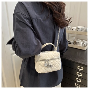 Détail d'un petit sac matelassé blanc avec bandoulière chaîne et pendentif fleur en métal