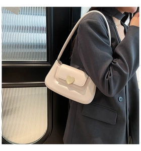 Detail of creamy white leather handbag with heart-shaped gold buckle worn on shoulder