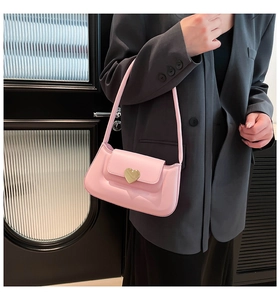 Detail of pink faux leather baguette bag with a gold heart clasp on a shoulder strap