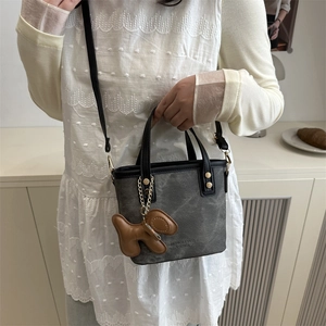 Minimalist grey bucket handbag with puppy charm and black shoulder strap on female model