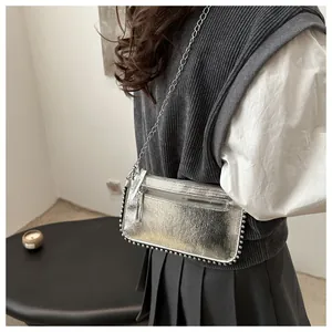 Detail of silver metallic crossbody bag with stud trim and chain strap on model