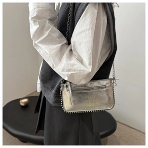 Close-up of silver envelope crossbody bag with metallic studs and chain strap detail