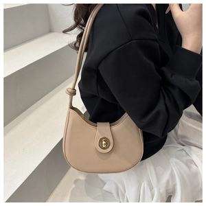 Modèle portant un sac hobo beige en forme de croissant avec fermoir rotatif doré chic