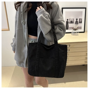 Detail of black corduroy tote bag showing large capacity and textured fabric on shoulder