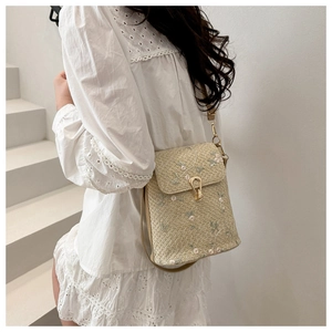Détails de broderies florales et du fermoir en métal doré sur le sac en paille tissé