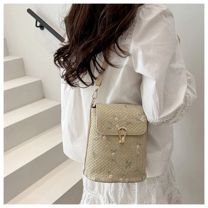 Dettaglio borsa a secchiello in paglia beige con ricami floreali e chiusura girevole dorata