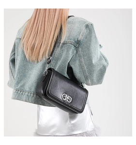 Detail of black leather small square bag with silver clasp worn on model shoulder